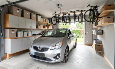 Garage résidentiel bien aménagé avec une voiture au centre, des rangements muraux, des étagères, des bacs et un espace de circulation dégagé.